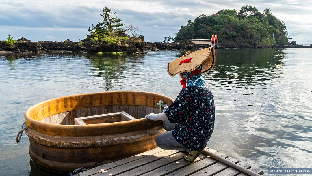 Femme en tenue traditionnelle devant une barque à Sado